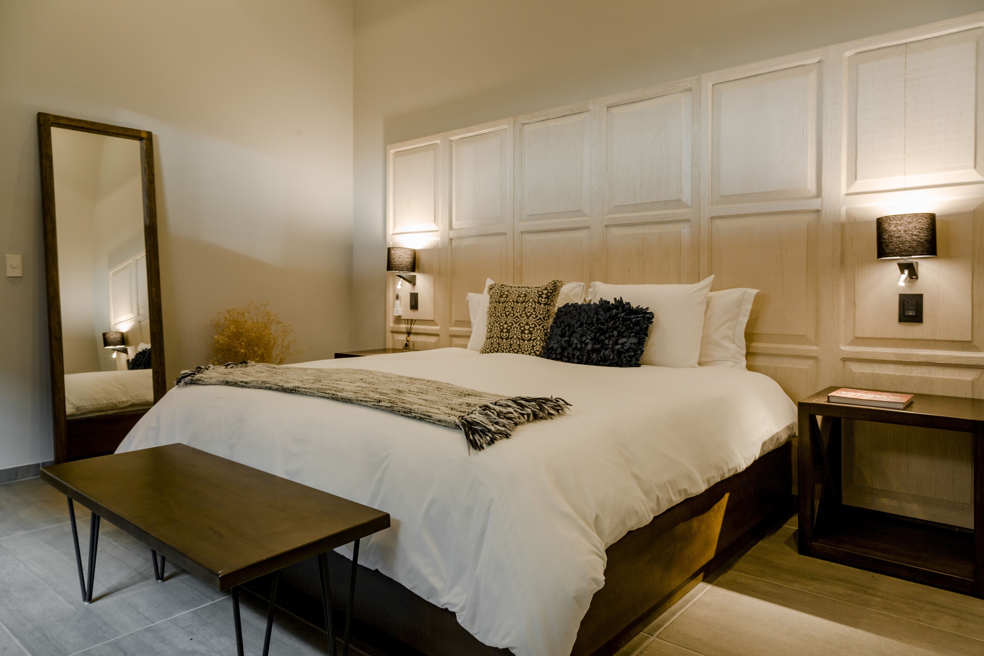 Un dormitorio con una cama grande, mesitas de noche, un espejo y lámparas fijadas a la pared.