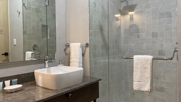 Un baño moderno con ducha de vidrio, lavamanos blanco y un espejo grande.