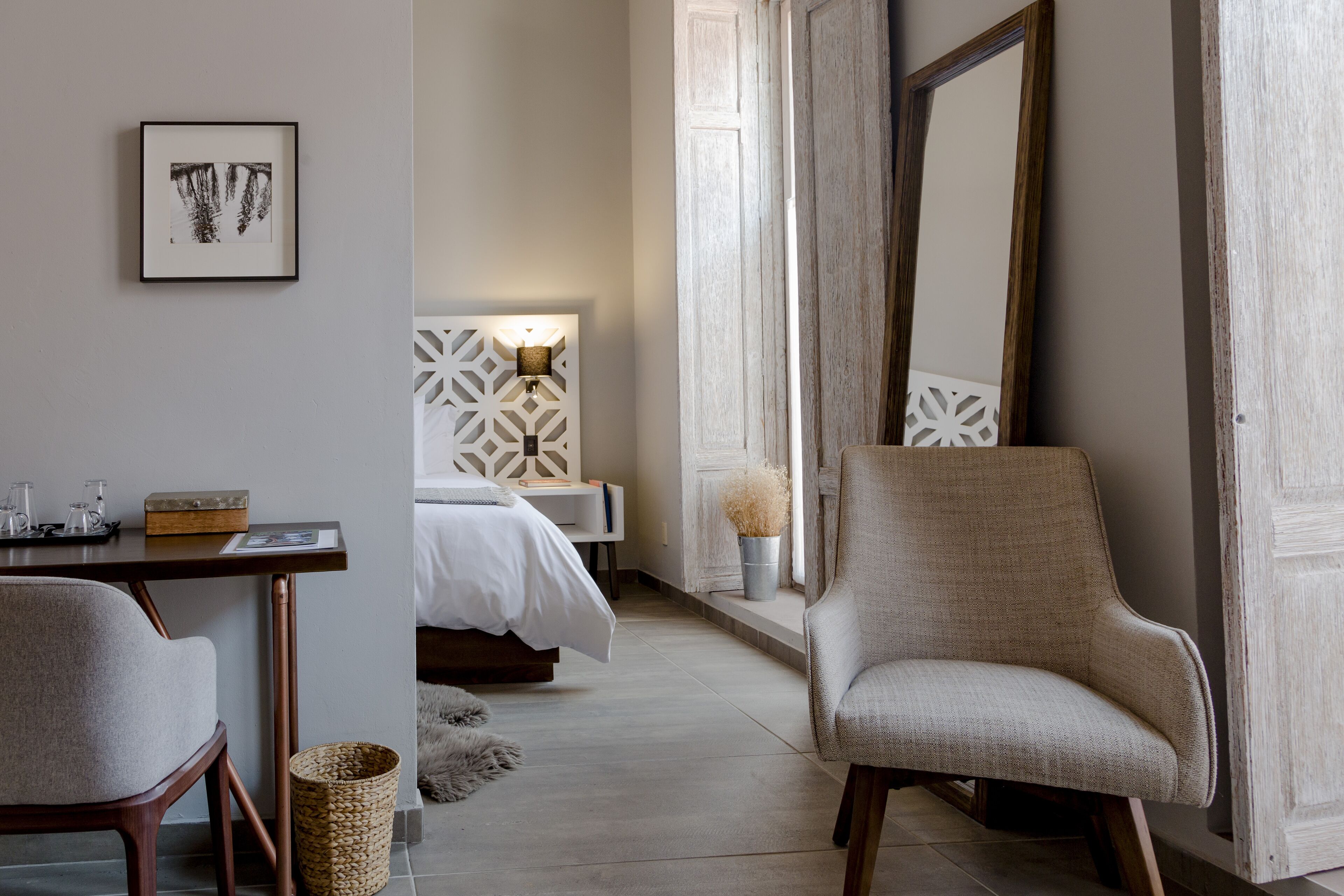 A hotel room with a bed, a chair, a desk, a lamp, and a large mirror.