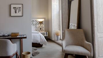 A hotel room with a bed, a chair, a desk, a lamp, and a large mirror.