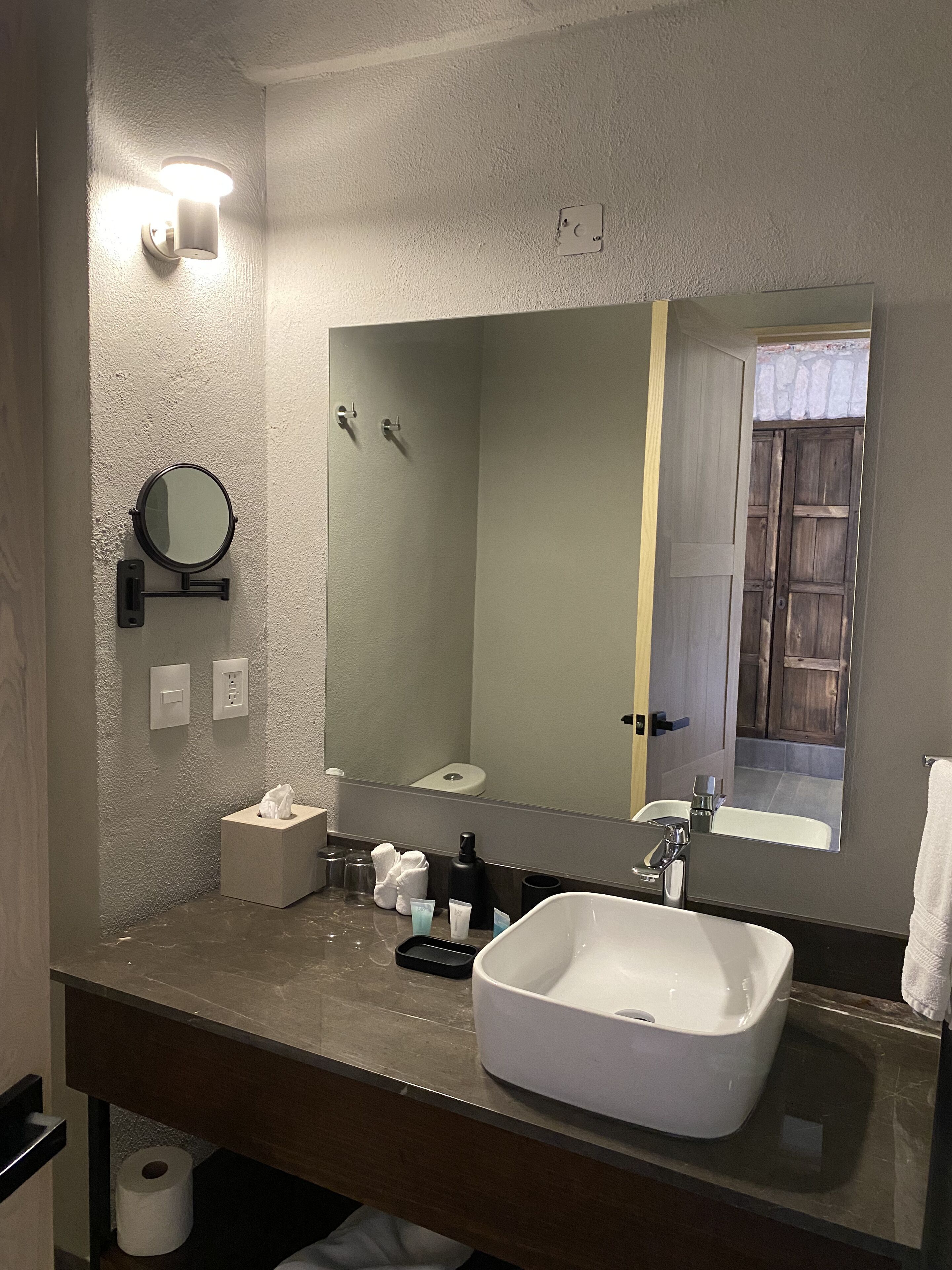A modern bathroom with a large mirror, a white sink, and a towel dispenser.