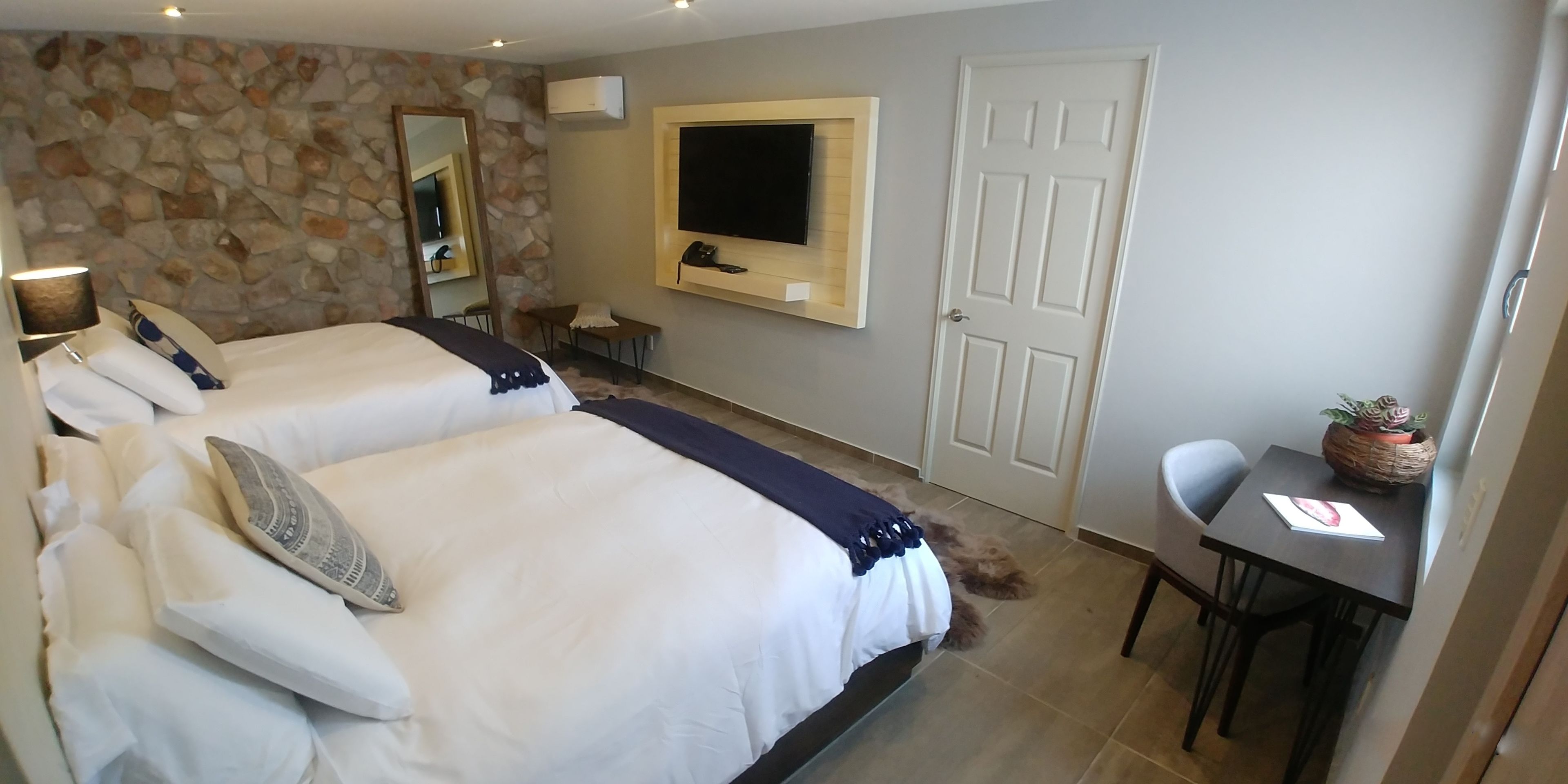 Habitación de hotel con dos camas, un escritorio, una silla, un televisor y una pared de piedra.