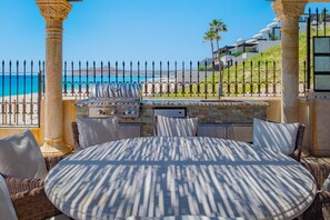 An outdoor seating area with a grill, wicker furniture, and a view of the beach and ocean. - Gated Beach Front,Daily Housekeeping,Breakfast Service,Backyard OasisHot TubPool (Cabo San Lucas)