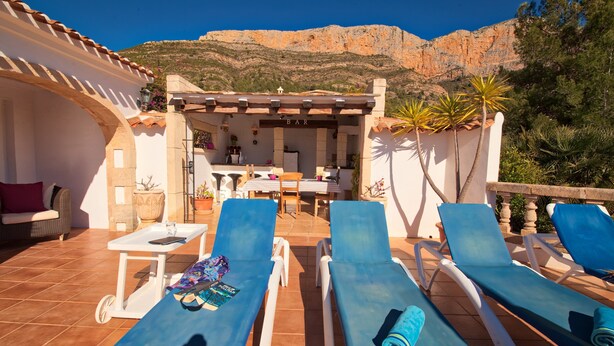 Une terrasse dotée de chaises longues, d’un espace bar et offrant une vue sur un paysage montagneux.