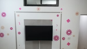 A living room with a TV mounted on a wall, a wooden cabinet below, and decorative wall stickers. - PRETTY T3 EQUIPPED COCODY (Cocody)