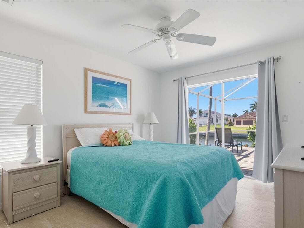 A bedroom with a bed, a ceiling fan, a window, and a view of the outside.