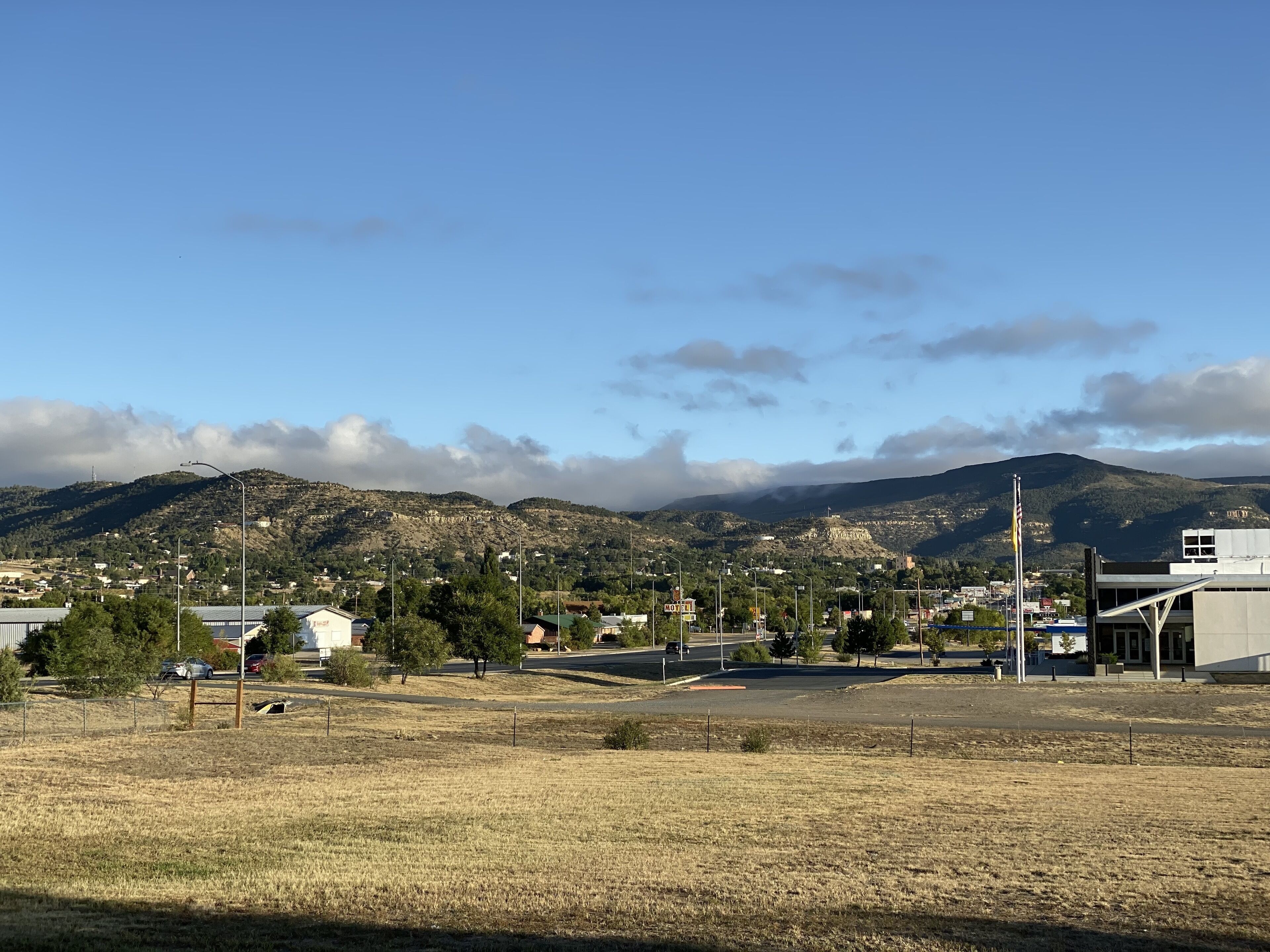 A town with a mountain backdrop, featuring a mix of residential and commercial buildings, a parking lot, and a clear sky.