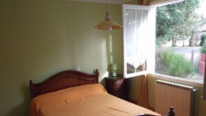 Una camera da letto con un letto di legno, una finestra vista sul verde e un termosifone.