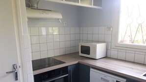 Una cucina compatta con mobili bianchi, un forno a microonde integrato, una lavastoviglie e un piano cottura.