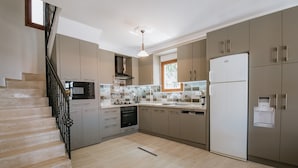 A modern kitchen with a built-in oven, microwave, and refrigerator. There is a window above the sink and a staircase on the left. - Spacious Villa with WiFi, A/C,  Private Pool and Rooftop Terrace
Licence 07-540  (Kalkan)