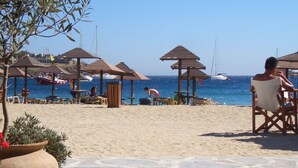 Een strand met houten parasols, een pad van stenen en boten op het water.