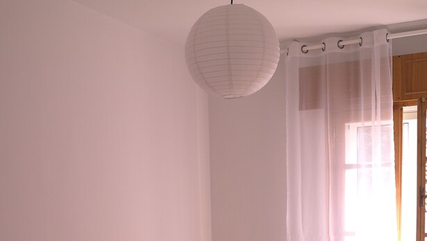 A bedroom with two beds, each with a white bedspread and a yellow pillow. There is a white lamp on one bed and a white towel folded on the other. A white paper lantern hangs from the ceiling, and a sheer curtain is drawn across a window. - In the historic center of Ourense, it is ideal for families or groups  (Ourense)