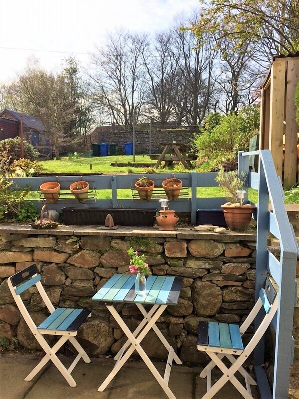 A patio with two wooden chairs and a table, surrounded by stone walls and potted plants.