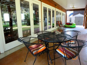A covered patio with a metal table and chairs, a sliding glass door, and a view of a backyard. - Waterfront rental, park-like setting, 2 Kayaks. 3 OR MORE NIGHTS GET 15% OFF. (Seguin)