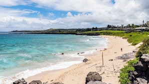 Une plage à l’eau turquoise et limpide, un rivage sablonneux, et quelques personnes profitant du soleil.