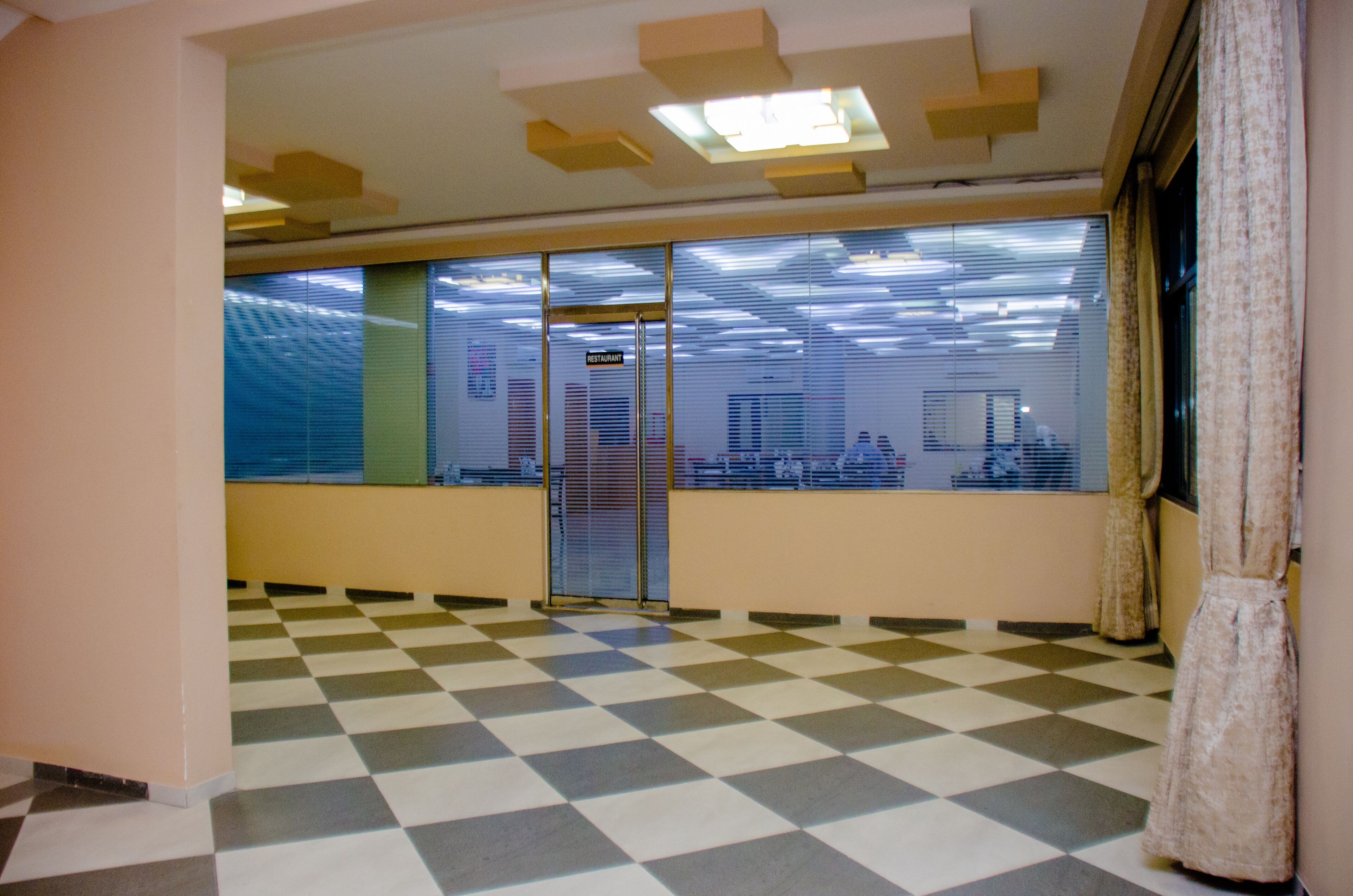 A hallway with a checkered floor, a door labeled "Restaurant," and a view through the windows.
