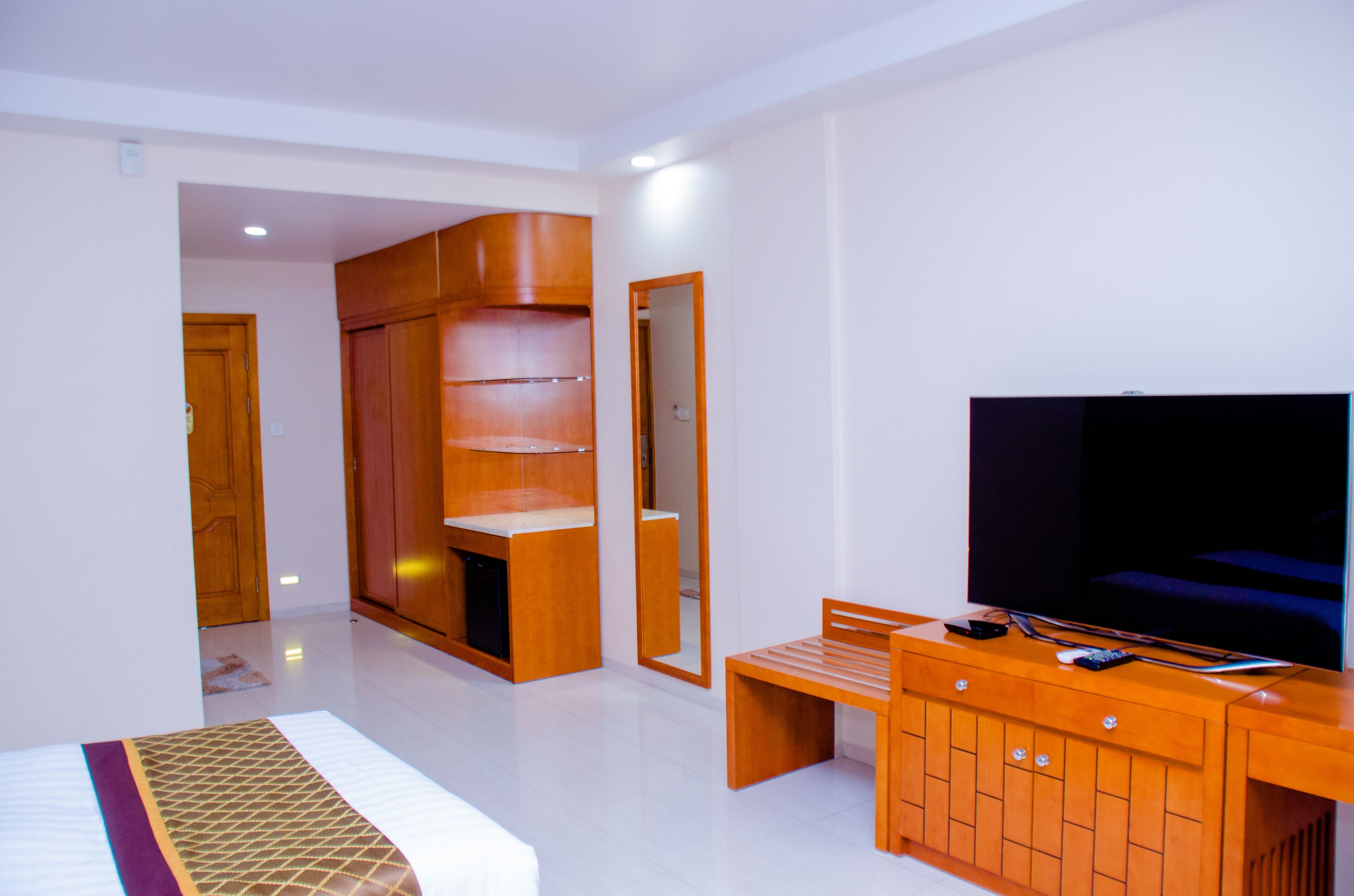 Un dormitorio moderno con cama, armario de madera, televisor y un banco.