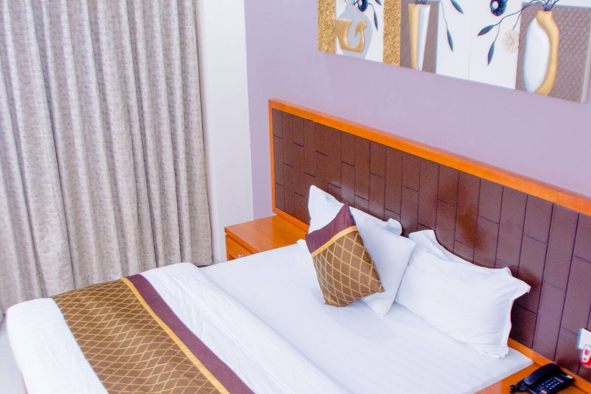 Una habitación de hotel con una cama, una mesita de noche, un teléfono y una pared decorada con obras de arte.