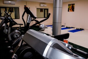 Un gimnasio con equipo de ejercicio, un espejo grande y una zona de colchonetas azules.