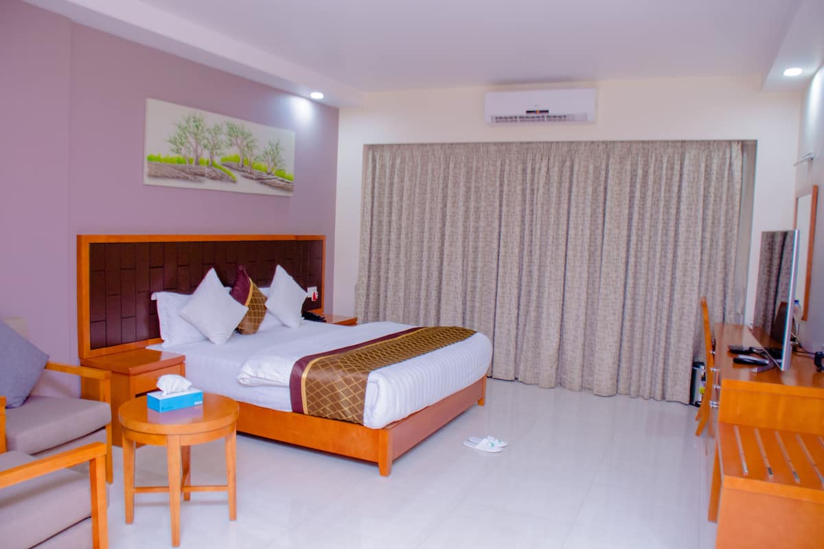 Habitación de hotel con una cama grande, un escritorio, una silla, una mesita y un ventanal con cortinas.
