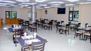 Un comedor amplio con varias mesas y sillas, un pilar grande y un televisor montado en la pared.