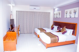 Habitación de hotel con dos camas, un escritorio, una silla y un ventanal con cortinas.