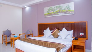 Una habitación de hotel con una cama grande, cabecera, mesita de noche, una silla y una pequeña mesa.