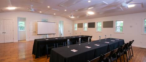 A conference room with a long table, chairs, ceiling fans, and windows.