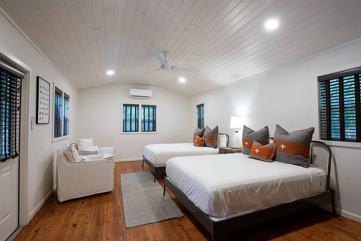 A hotel room with two beds, a sofa, a desk, and a window with blinds.