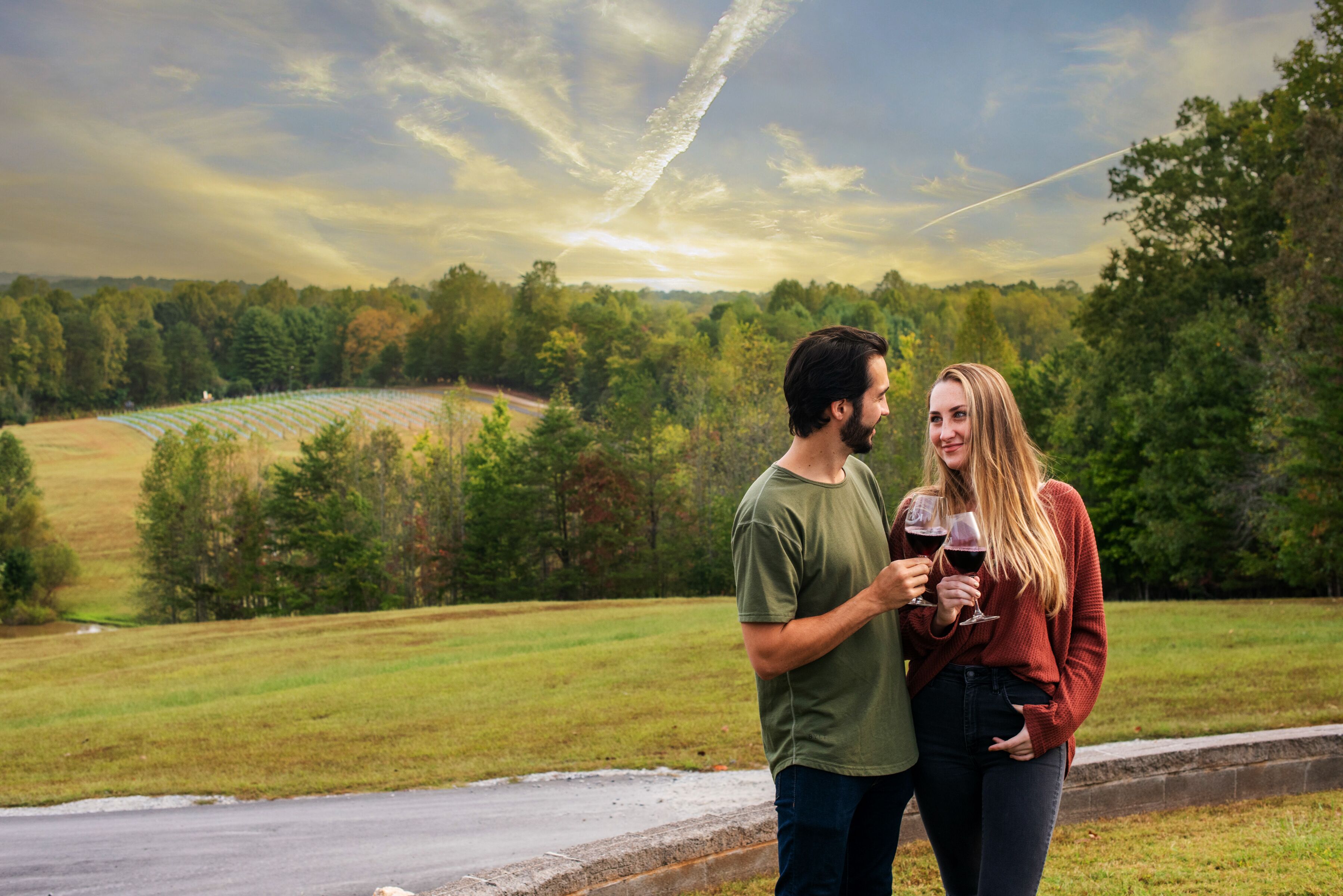 A couple standing by a road with a scenic view of a field and trees in the background.