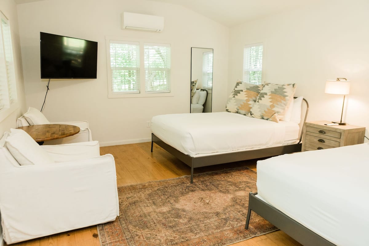 A modern bedroom with a bed, bedside tables, a TV, and a window with blinds.
