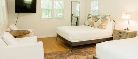 A modern bedroom with a bed, bedside tables, a TV, and a window with blinds.