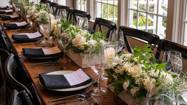 A long wooden table set for a formal event with chairs, glassware, and floral centerpieces. - Dahlonega Resort and Vineyard (Dahlonega)