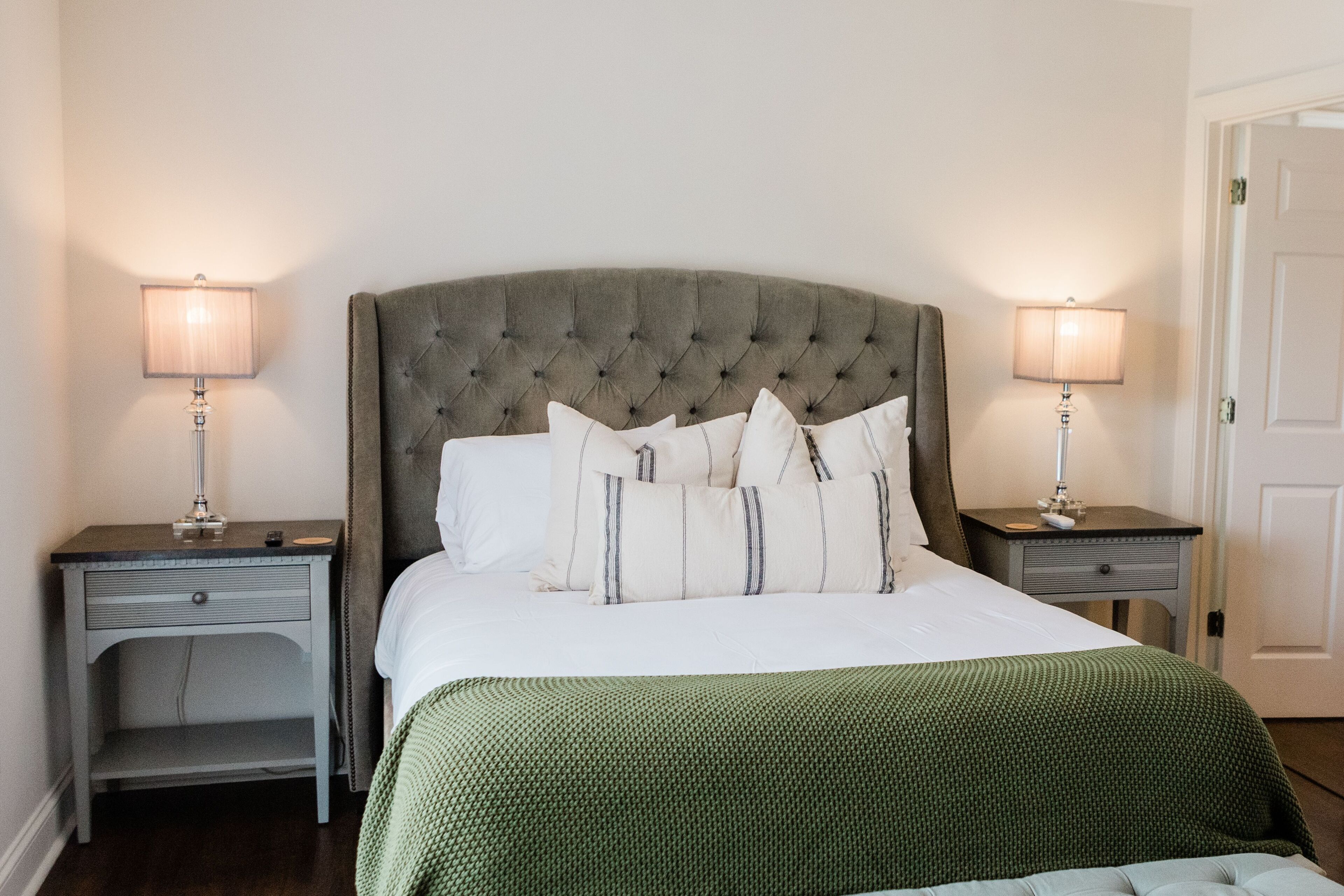 A neatly made bed with a tufted headboard, two bedside tables with lamps, and a green textured blanket.