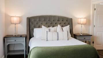 A neatly made bed with a tufted headboard, two bedside tables with lamps, and a green textured blanket.