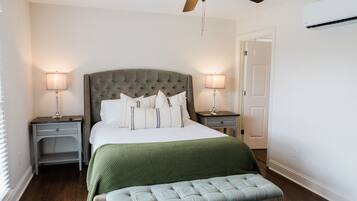 A bedroom with a tufted headboard, a green bedspread, two bedside lamps, a bench, and a ceiling fan.