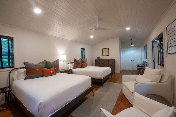 Quarto com duas camas, cômoda, cadeira e ventilador de teto.