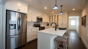 A modern kitchen with white cabinetry, stainless steel appliances, a central island with stools, and pendant lighting. - Dahlonega Resort and Vineyard (Dahlonega)