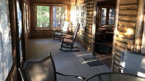 Ein Holzblockhaus-Interieur mit einer Veranda, Schaukelstühlen und einem Tisch.