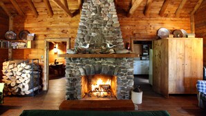 Ein gemütliches Blockhaus-Interieur mit Kamin aus Naturstein, Holzbalken und einer rustikalen Küchenzeile.