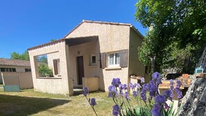 A house with a tiled roof, a small porch, and a garden with purple flowers.