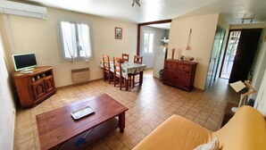Un coin repas comprenant une table, des chaises, un meuble en bois, un téléviseur et une fenêtre avec des rideaux.