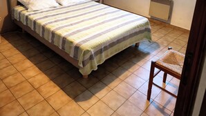 Une chambre à coucher avec un lit, une table de chevet avec une lampe, une fenêtre avec des rideaux et un radiateur.