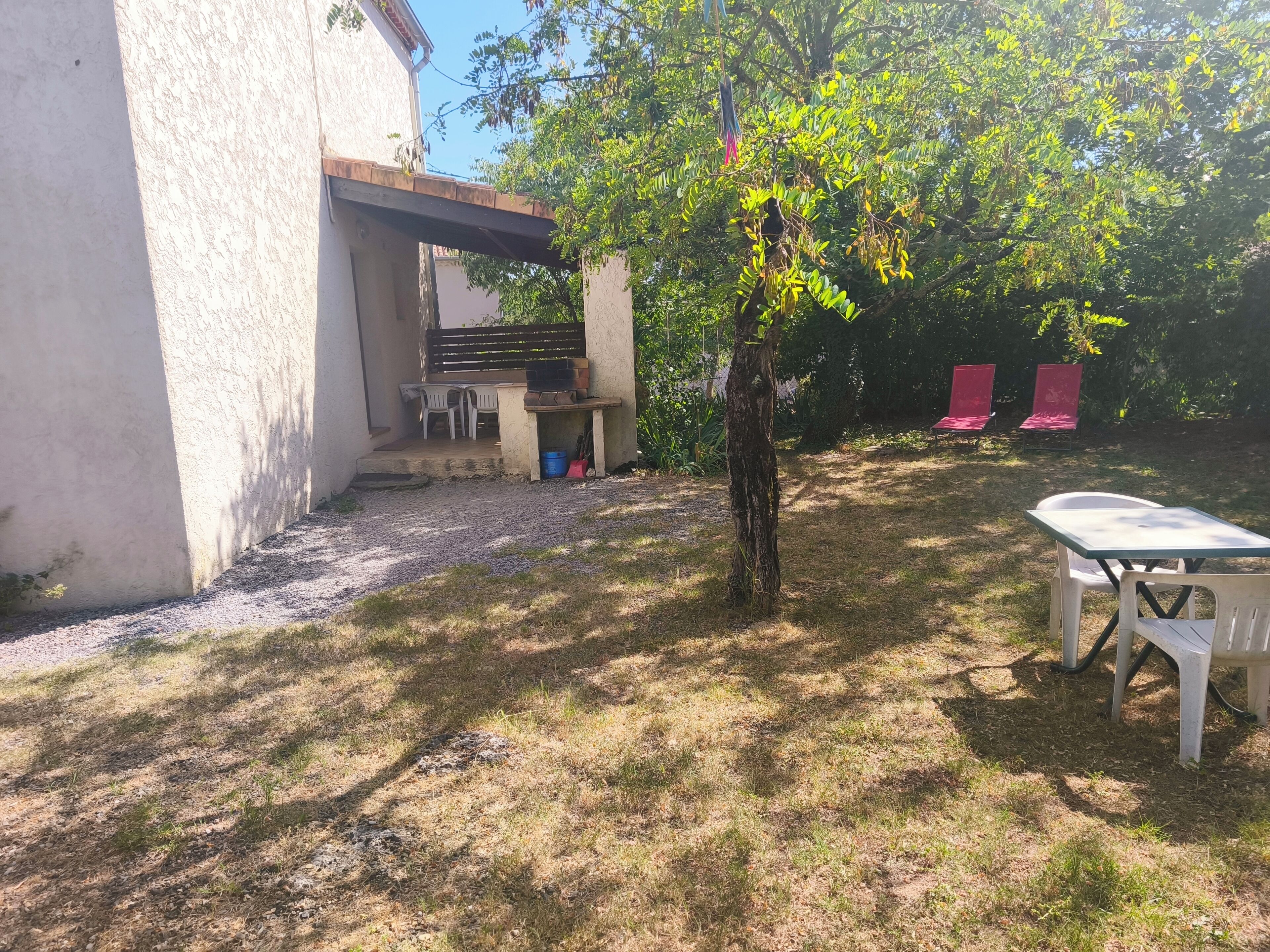 A patio area with a table and chairs, a small tree, and a building with a balcony.