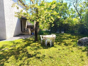 Un patio con una mesa, sillas, un árbol y una estructura de piedra.