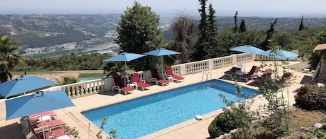 A pool area with lounge chairs and umbrellas, surrounded by greenery and overlooking a scenic landscape.