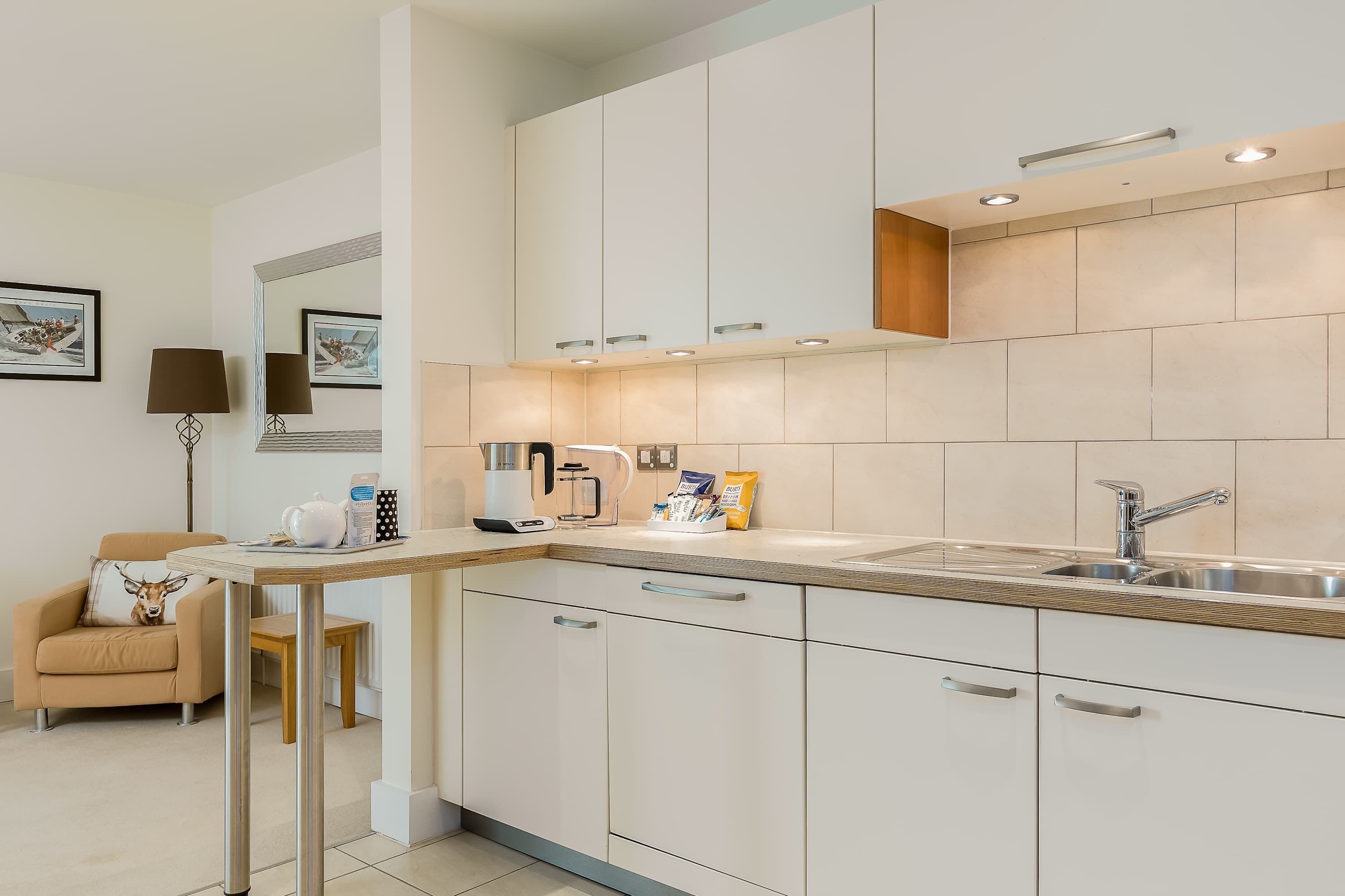 A modern kitchen with white cabinets, a stainless steel sink, and a wooden countertop.