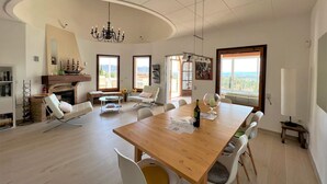 A spacious dining area with a wooden table, white chairs, and a chandelier. - Holiday house - privatpool + glass fiber, views + aircondition, Wallbox (3,7kW) (El Mas Fumats)