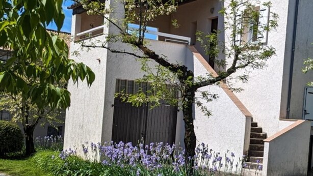 Een modern gebouw met een witte gevel, een zichtbare trap en een tuin met paarse bloemen.
