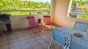 Een balkon met een tafel, stoelen, een barbecue en een bloempot.
